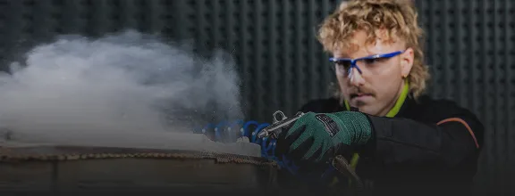 Person arbeitet mit Druckluftwerkzeug an einem industriellen Bauteil, Dampf steigt auf.